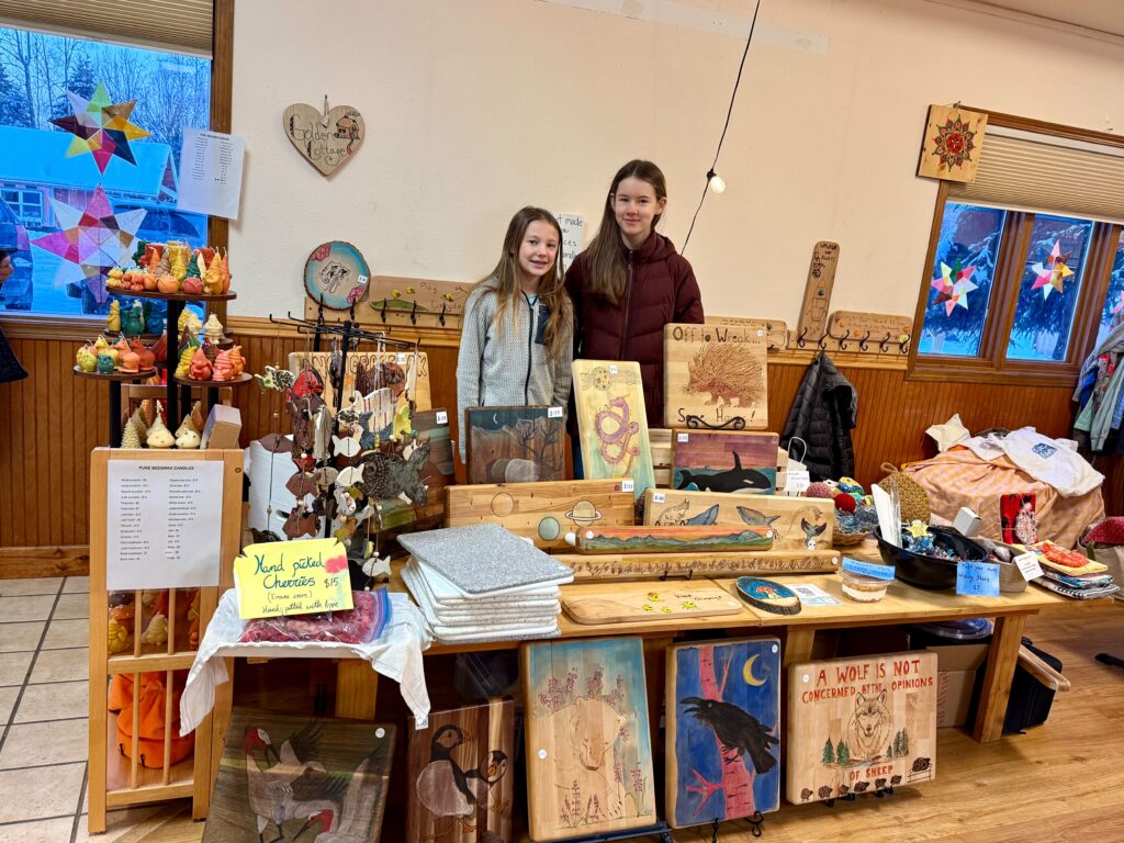Waldorf students standing next to a table of art made by students at the winter faire